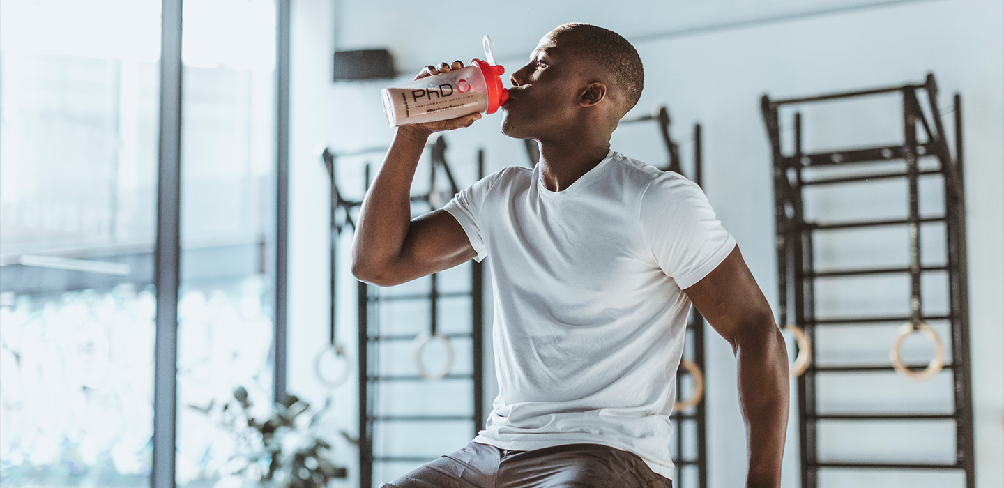 Man drinking a protein shake sitting in a gym setting