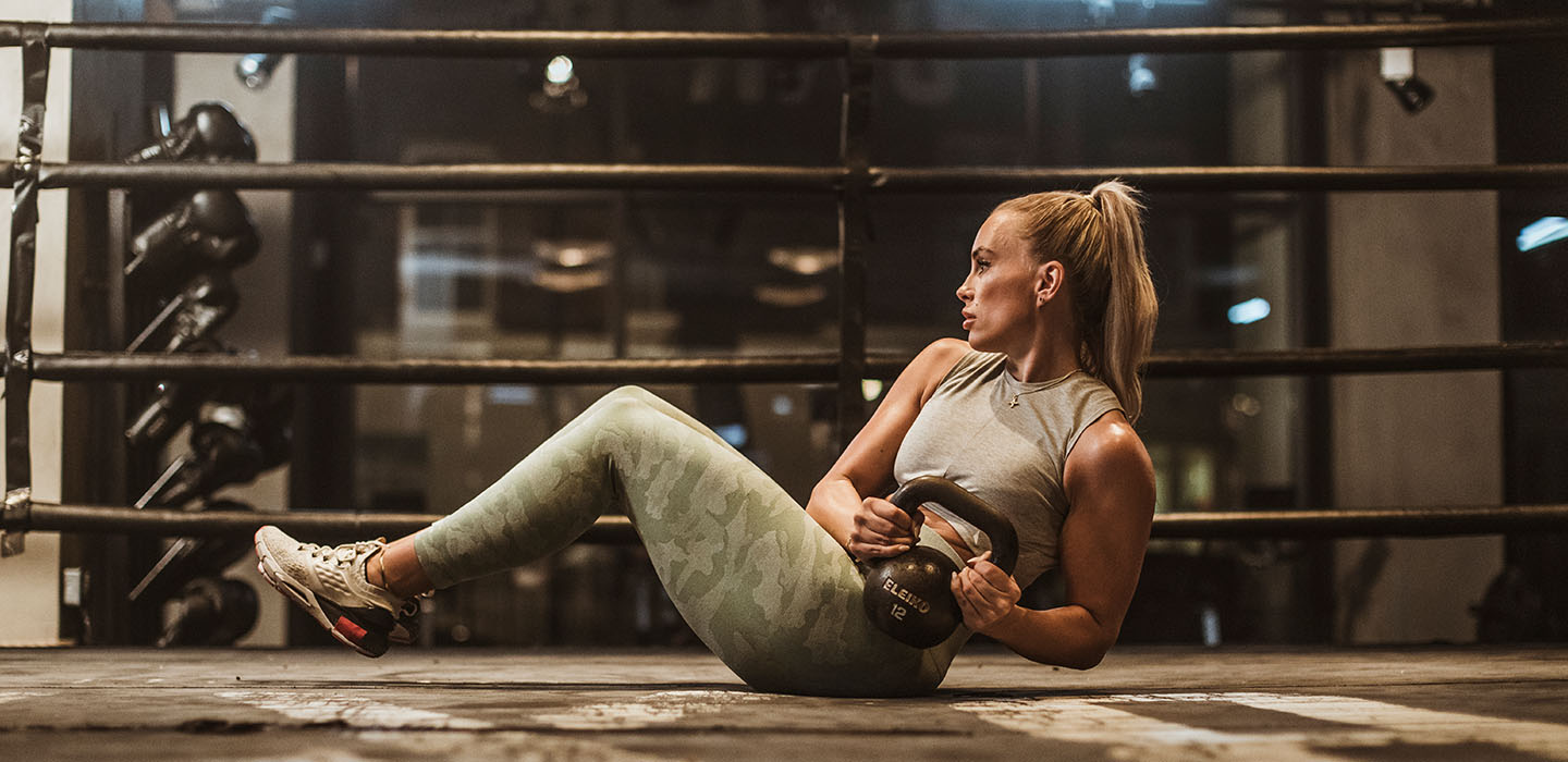 Lady working out in a boxing ring using a kettle bell to perform an ab exercise