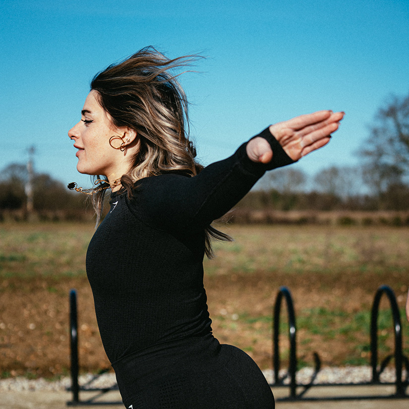 Woman in workout attire posing like she is flying outside